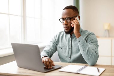 Ciddi bir siyahi iş adamı cep telefonuyla konuşuyor. Modern Ofiste İşyerinde Dizüstü bilgisayar kullanıyor. İş İletişim ve Müzakere Cep Telefonu Konsepti