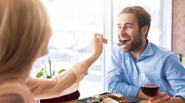 Olumlu genç çift kafede romantik bir akşam yemeği yiyor, doğum gününü kutluyor, birbirlerini besliyor, şarap içiyor. Güzel bayan erkek arkadaşına kahve dükkanında taze salata veriyor.