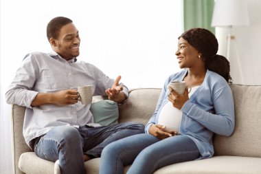 Siyah bir çiftin kanepede oturup, evde çay içmelerini sohbet etmelerini ve aralarındaki boşluğu kopyalamalarını beklemek çok keyifli. Neşeli Afro-Amerikan hamile ailesi oturma odasında dinleniyor.