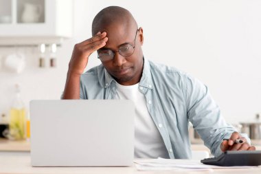 Hesap makinesi ve dizüstü bilgisayar kullanarak, vergileri hesaplayarak, aylık giderleri ve faturaları kontrol ederek, evde mutfak içlerinde oturarak,