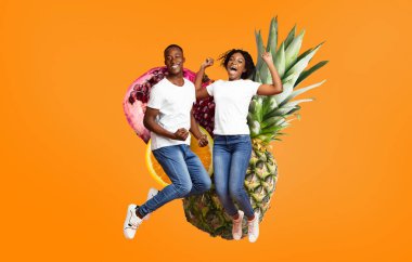 İki genç yetişkin, ananas ve nar gibi tropikal meyvelerin yer aldığı parlak turuncu bir arka planda heyecanla zıplıyorlar. Neşeleri yaz eğlencesinin ve arkadaşlığın özünü yansıtıyor..