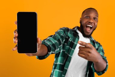 Mobil Telefon Ekranını Kameraya Gösteren ve Sarı Stüdyo Arkaplanındaki Yeni Başvuru Pozunu Gösteren Heyecanlı Siyah Adam. Akıllı Telefon Konsepti için harika bir uygulama. Mockup, Cep Telefonuna Odaklan