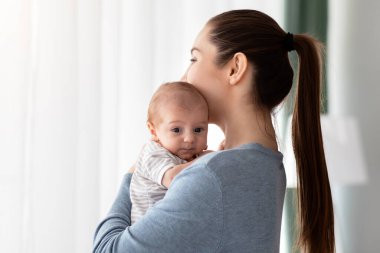 Annelik Ruhsal Sağlık Sorunları. Genç bir kadının kucağında sevimli bir bebek, pencerenin yanında duruyor, Milenyum Annesinin doğum sonrası depresyondan muzdarip olması, Boşluğu Kopyalaması