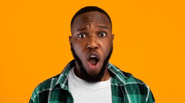 Shocked African Guy Looking At Camera Frowning Posing With Opened Mouth Standing On Yellow Studio Background. Emotional Black Man Expressing Shock Emotion. Panorama