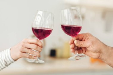 Romantik çift evde yemek yiyor, aşk, ilişki ve aşk konsepti. Modern mutfağın içinde kırmızı şarap kadehleri tutan mutlu çift, yakın çekim, fotokopi alanı, kırpılmış