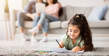 Aile içi hafta sonu. Ailesi dijital tabletle kanepeye uzanmış, evde vakit geçirmekten hoşlanan, seçici bir şekilde çocuğa odaklanan sevimli, küçük bir kız.