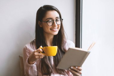 Bir fincan çayla kaygısız latin bayan pencerenin yanındaki kafede dinlenirken en sevdiği kitabı okuyor, boş bir alanda. Keyifli zaman ve eğlence yaşam tarzı konsepti