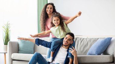 Portrait Of Happy Middle Eastern Parents Bonding With Their Child At Home, Happy Arab Family With Daughter Having Fun In Living Room, Playing And Laughing, Enjoying Spending Time Together, Free Space