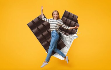 Neşeli, sıradan kıyafetler giyen bir kadın parlak sarı bir arka planın önüne heyecanla atlıyor. Etrafı çikolata parçalarıyla çevrili. Neşe ve hoşgörü simgesi..
