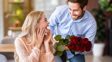 Özel bir olayı kutluyoruz. Romantik genç adam, kafedeki heyecanlı kız arkadaşına bir buket kırmızı gül sunuyor. Lokantada Sevgililer Günü için çiçekli güzel bir milenyum çifti.