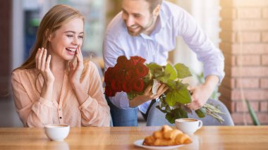 Sevecen bir milenyum erkeği sevgilisine sürpriz yapıp kafede bir buket çiçek veriyor. Sevgili genç çift yıldönümünü, doğum gününü ya da sevgililer gününü kantinde kutluyorlar.