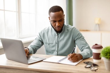 Bilgisayarda çalışan Afrikalı iş adamı ve modern ofiste oturan iş raporlarını not alan biri. Girişimcilik Kariyeri, Yaşam Tarzı ve Meslek Konsepti