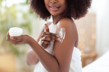 Genç siyahi bir kadının vücuduna krem sürdüğü, duştan sonra cildini pohpohladığı, yakın plan. Tanınmayan Afrikalı Amerikalı kadın günlük güzellik rutini yapıyor.