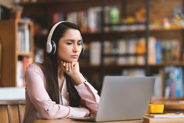 Çevrimiçi eğitim kavramı. Kafede bilgisayar ve kulaklık kullanarak internet üzerinden çalışan konsantre Latin kadın, kopya alanı. Arap bayan öğrenci çevrimiçi ders alıyor, laptop ekranına bakıyor.