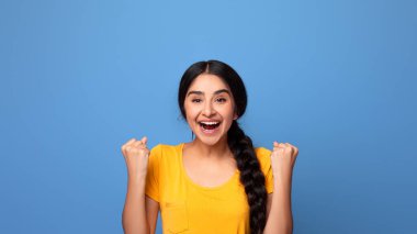 Evet, Başarı Konsepti. Heyecanlı genç Hintli kadın tezahürat yapıyor ve çığlık atıyor, zaferi kutluyor. Duygusal bunalmış kadın bağırıyor ve yumruklarını sallıyor, mor arka planda izole edilmiş.