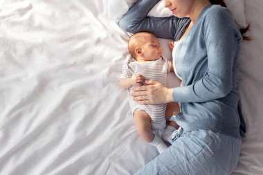 Bebekle birlikte uyumak. Genç bir kadın, tatlı yeni doğmuş çocuğuyla yatakta kestiriyor. Yeni doğmuş bebeğini seven bir anne. Gündüz vakti birlikte uyurken bebeğini kucaklıyor.