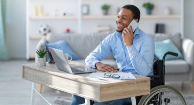 Tekerlekli sandalyedeki siyahi adamın evde dizüstü bilgisayarla çalışırken telefonla konuşması çok keyifli. Genç işadamı cep telefonuyla müşteriyle konuşuyor.