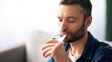 Sağlıklı yaşam tarzı, su içmesi, hidrasyon konsepti. Orta yaşlı, sakallı, bir bardak su içen, evinde tatlı su içen, fotokopi alanı olan bir adam.