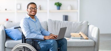 Tekerlekli sandalyedeki özürlü siyahi adam dizüstü bilgisayar kullanıyor, evden çalışıyor, yer kopyalıyor. Milenyum Afrikalı Amerikalı adamın işi ya da interneti var.