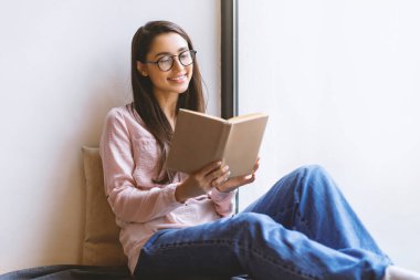 Gözlüklü mutlu Latin bayan en sevdiği kitabı okuyor, gündüz vakti pencerenin yanındaki kafede dinleniyor, boş yer var. Boş zaman, eğitim ve kentsel yaşam tarzı kavramı