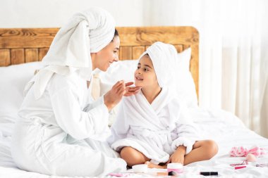 Neşeli anne ve kız makyaj ürünleri ile oynuyor evde dinlenirken, kafalarına bornoz ve havlu giyiyorlar, güzel bir günü birlikte geçiriyorlar, boşluğu kopyalıyorlar.