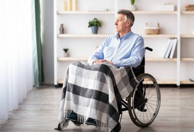 Üzgün, sakat, yaşlı bir adam, tek başına bir huzurevinde oturup pencereden bakıyor. Fiziksel engelli, mutsuz ve yalnız hisseden yaşlı bir erkek hasta.