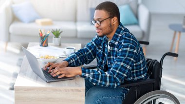 Özürlü insanlar için internet işi. Tekerlekli sandalyedeki siyah adam evdeki uzaktan kumanda için dizüstü bilgisayar kullanıyor. Millennial Man 'in internette iş görüşmesi var, video görüşmesi yapıyor.