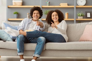 Covid-19 'daki yalnızlık ve favori film sırasında evde birlikte eğlenmek. Binlerce yıllık Afro-Amerikan karı-koca TV 'yi izleyip, parmakla göstererek, oturma odasındaki kanepede oturuyor.