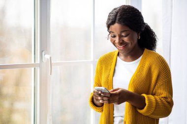 Evdeki pencerenin kenarında duran, akıllı telefon kullanan, arkadaşlarıyla ya da sevgilileriyle sohbet eden, fotokopi alanı olan bir panorama. Cep telefonu tutan mutlu Afrikalı Amerikalı kadın