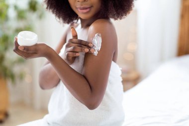 Tanımlanamayan siyahi kadın sabahları evde duş aldıktan sonra omzuna krem sürüyor. Afro-Amerikalı bir kadının güzellik prosedürü uyguladığı, kendini evde şımarttığı görüntüler.