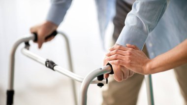 Tanımlanamayan yaşlı bir adam Walker 'ı kullanıyor, genç bir doktor huzurevinde ona destek oluyor ve yardım ediyor. Emeklinin yürüyüşü, bakıcısı elini tutuyor, yakın plan.