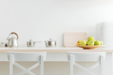 Sağlıklı yiyecekler, kahvaltı ve modern ev içleri. Mobilyalar, tabakta elmalar, tabaklar, küçük buzdolabı, beyaz duvar arkaplanı, minimalist mutfak, boş alan, bulanık, hiç kimse