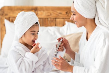 Aynaya bakan, ruj süren, annesiyle güzel bir gün geçiren, kafalarına bornoz ve havlu takan, yatak odasının içini kapatan güzel bir kız.