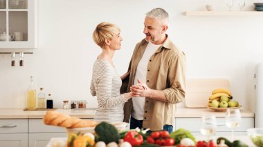 Yıldönümü, romantizm ve randevunun tadını çıkar. Salata yapmak için taze taze sebzeler, masada bir bardak hafif şarap. Mutfakta dans eden mutlu yetişkin çift, boş alan.