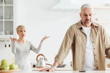 Tartışmalar, tartışmalar, skandallar, çift ilişkilerinde sorunlar ve kendini tecrit sırasında evde taciz. Kızgın orta yaşlı eş, beyaz mutfak iç dekorasyonunda üzgün yaşlı adama bağırıyor.
