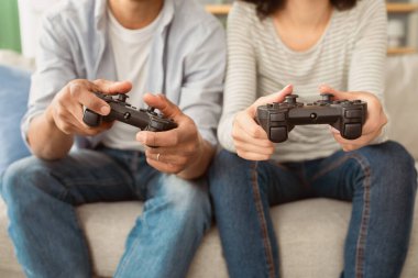 Evde oynayın ve covid-19 sırasında birlikte eğlenin. Milenyum Afrikalı Amerikalı bir adam ve joystickli bir kadın çevrimiçi bir oyun oynuyorlar, rahat oturma odasındaki kanepede oturuyorlar, kırpılmış, kopyalanmış