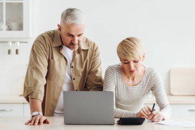 Hesaplar, krediler, ipotekler ve vergiler. Masrafları hesaplayan ve minimalist beyaz mutfak, panorama, ücretsiz alan, dizüstü bilgisayar ve not defteri ile ödeyen son sınıf öğrencisi kadın ve erkek.