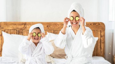 Mutlu aile ferdi genç anne ve küçük kızı salatalıklı gözler ve havlular yatakta oturuyor, spa yapıyorlar. Anne, küçük kızıyla güzel bir gün geçiriyor. Yatak odasının içi.
