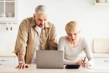 Hesaplar, krediler, ipotekler ve vergiler. Masrafları hesaplayan ve minimalist beyaz mutfak, panorama, ücretsiz alan, dizüstü bilgisayar ve not defteri ile ödeyen son sınıf öğrencisi kadın ve erkek.