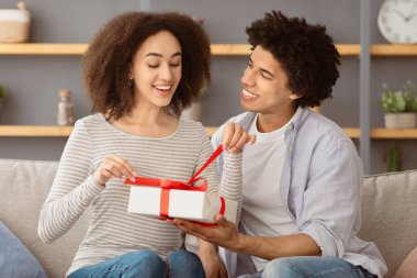 Tatil ve kovid 19 karantina ve ev partisi sırasında özel bir randevu. Gülümseyen Afrikalı genç Amerikalı kadın, kadın iç mekanda kırmızı kurdele, serbest alan hediye ediyor.