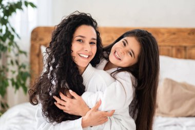 Güzel annesine sarılan, beyaz bornoz giyen, evinde yatağında oturan, fotokopi çeken tatlı küçük bir kız. Mutlu kıvırcık kız annesiyle vakit geçirir, birlikte güzel bir gün geçirir.