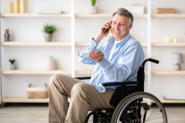 Tekerlekli sandalyedeki neşeli engelli adam huzurevinde akıllı telefon alıyor. Olumlu engelli erkek portresi arkadaşlarıyla ya da aileleriyle telefon görüşmesi yapıyor.