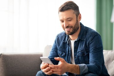 Evdeki modern cep telefonuyla koltukta oturan neşeli orta yaşlı bir adam arkadaşlarıyla sohbet ediyor, fotokopi çekiyor. Akıllı telefon kullanan, yeni mobil uygulamaları kontrol eden pozitif sakallı adam