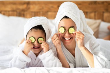 Mutlu aile ferdi genç anne ve kız salatalıklı gözler ve havlular yatakta uzanmış evde spa yapıyorlar. Anne, küçük kızıyla güzel bir gün geçiriyor. Yatak odasının içi.