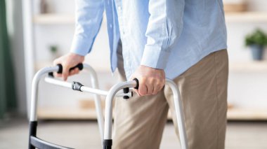 Evde çerçeveyle yürüyen yaşlı bir adamın görüntüsü, yakın plan. Tanımlanamayan son sınıf öğrencisi. Evinde dolaşmak için tıbbi ekipman kullanıyor. Profesyonel yardıma ihtiyacı olan engelli yaşlı kişi