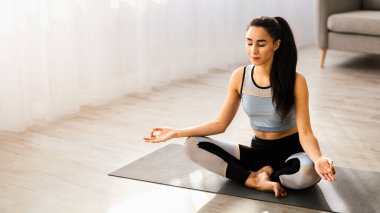 Kafkasyalı genç bir kadının, evde meditasyon yaparken, oturma odasında, fotokopi odasında Lotus 'ta poz verirken yüksek açılı görüntüsü. Yoga yapan bir kadın, sağlıklı bir yaşam tarzı olan.