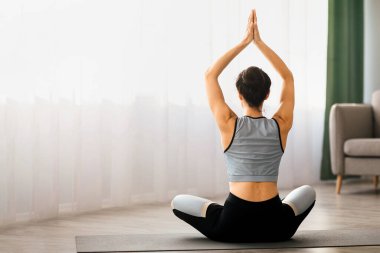 Evde yoga yapan genç bir bayanın dikiz ayarı namaste jesti, meditasyon ve fotokopi alanı ile ellerini kaldırması. Sportif esnek kadın yoga yapıyor, oturma odasının içinde.