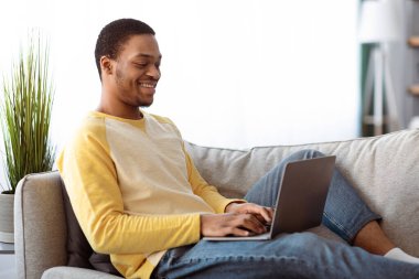 Evde dinlenirken, yan görüş ve kopyalama alanı kullanırken rahat bir siyah adam. Mutlu Afrikalı Amerikalı genç adam arkadaşlarıyla online ya da evden çalışan serbest çalışan