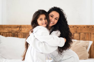 Mutlu anne ve çocuk güzel bir gün geçiriyor, yatakta oturuyor, kameraya sarılıyor ve neşeyle gülümsüyor, fotokopi çekiyor. Çok tatlı bir anne ve küçük kız bornozlu evde yatakta kaynaşıyorlar..