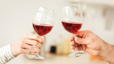 Romantik çift evde yemek yiyor, aşk, ilişki ve aşk konsepti. Modern mutfağın içinde kırmızı şarap kadehleri tutan mutlu çift, yakın çekim, fotokopi alanı, kırpılmış